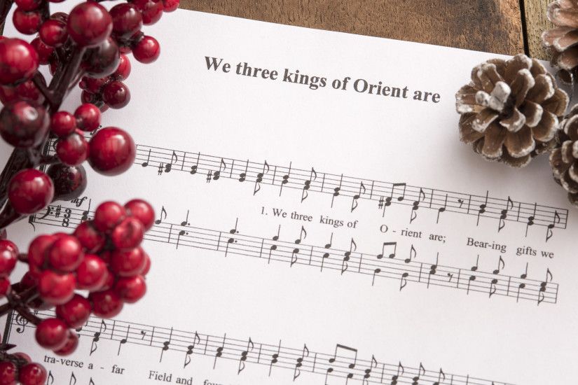 Christmas carol festive background with colorful red berries and pine cones  on a music score sheet