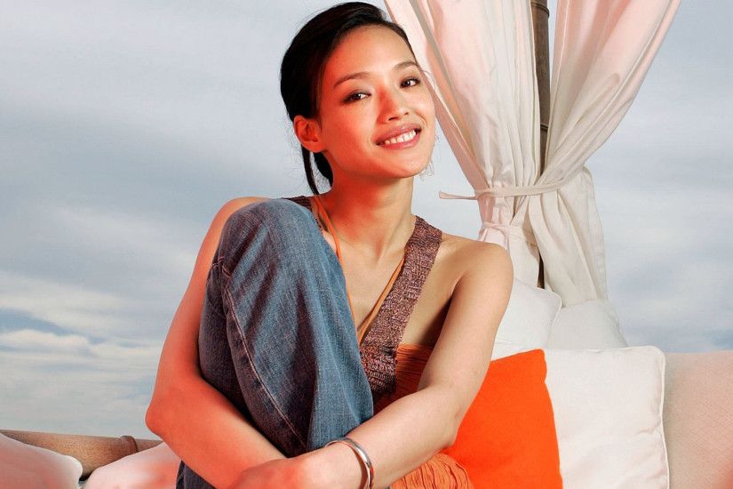 Shu Qi smiling with hands crossed on her leg wallpaper