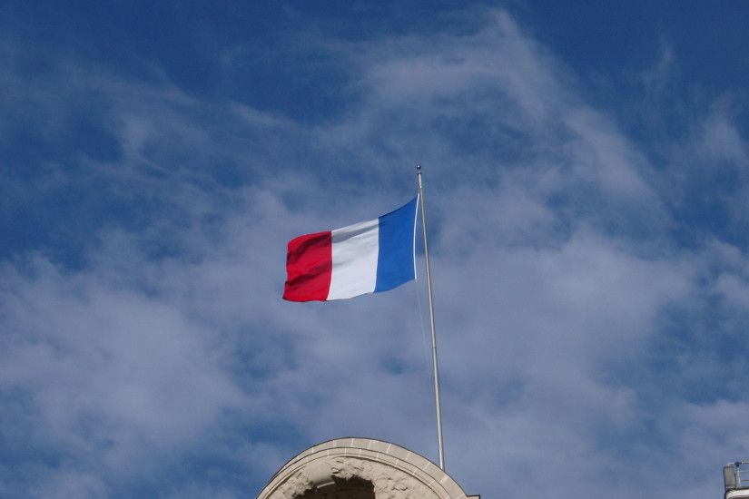 The Tricolor or French National Flag flying from a rooftop against a cloudy  hazy blue sky