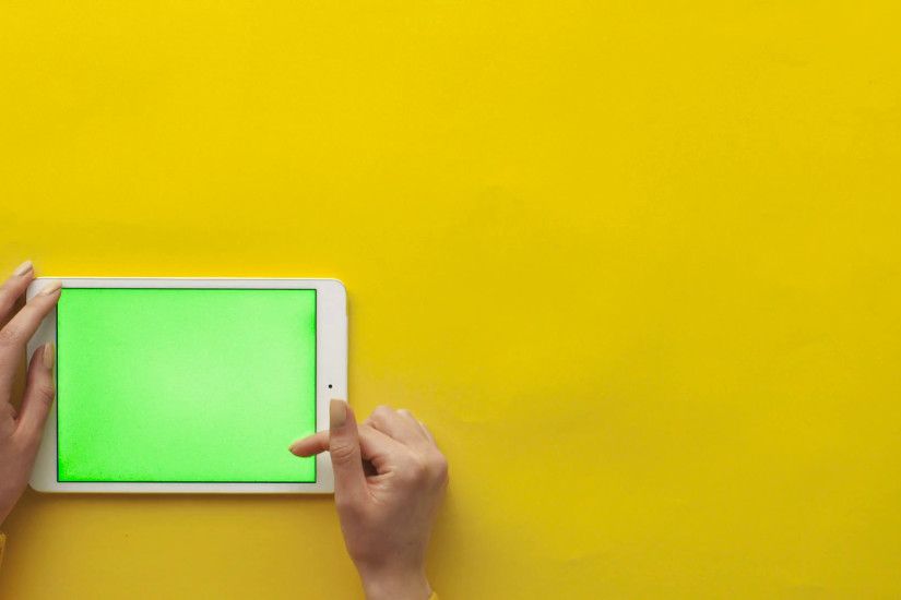 Female hands using white tablet computer with green screen on yellow  background. Woman scrolling pages, tapping on touch screen, surfing on the  internet.