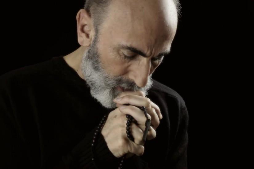Religious man praying trouble. A religious man praying God with a rosary in  his old wrinkled hands, appearing tormented, full of troubles. Black  background.