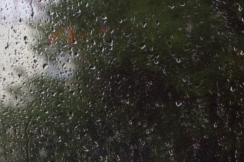 Raindrops falling on glass window with blurred green nature background.  Rainy day with focus on water drops running on wet windowpane with abstract  ...