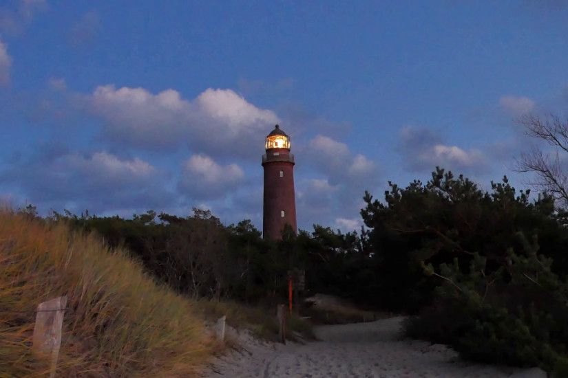 Shinning old lighthouse with dark clouds after sunset in background. Tower  illuminated with strong warning light. Lighthouse built from red bricks.
