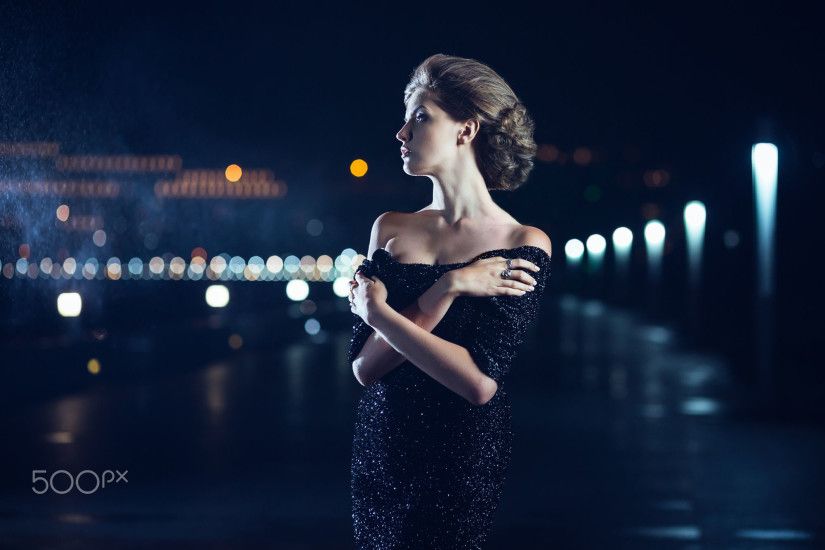 Beautiful woman in black dress posing on a city lights background