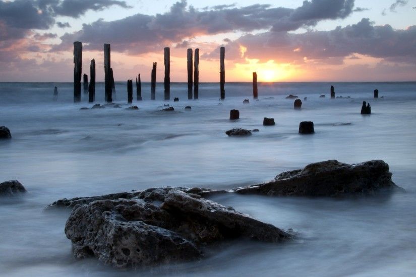 Wooden pillars standing tall towards the ocean sunset wallpaper