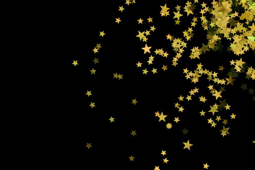 a scattering of yellow coloured glitter star shapes on a black backdrop