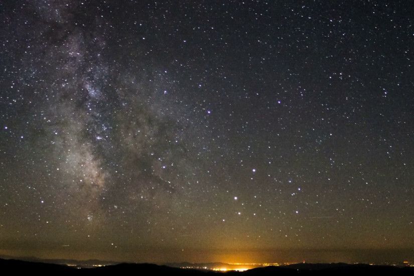 Milky Way Galaxy astronomy time lapse stars moving above mountain valley  light pollution near horizon bright