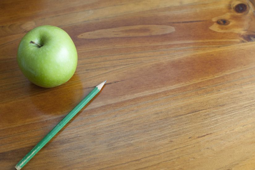 Schooled themed background of a wooden desk with a green apple and pencil