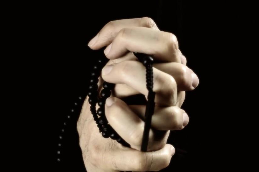 Hands praying black rosary. The wrinkled hands of an old man holding a  rosary and praying. Detail close-up shot. Isolated on black background.